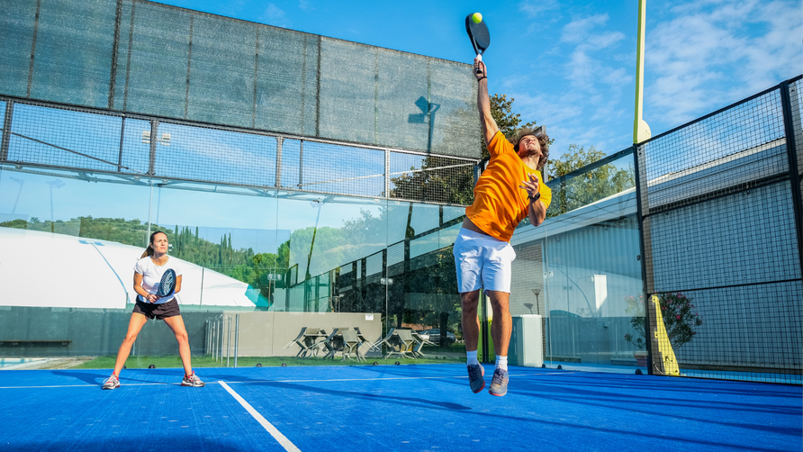 Ouder en kind spelen samen padel op een outdoor padelbaan, een sport die geschikt is voor het hele gezin