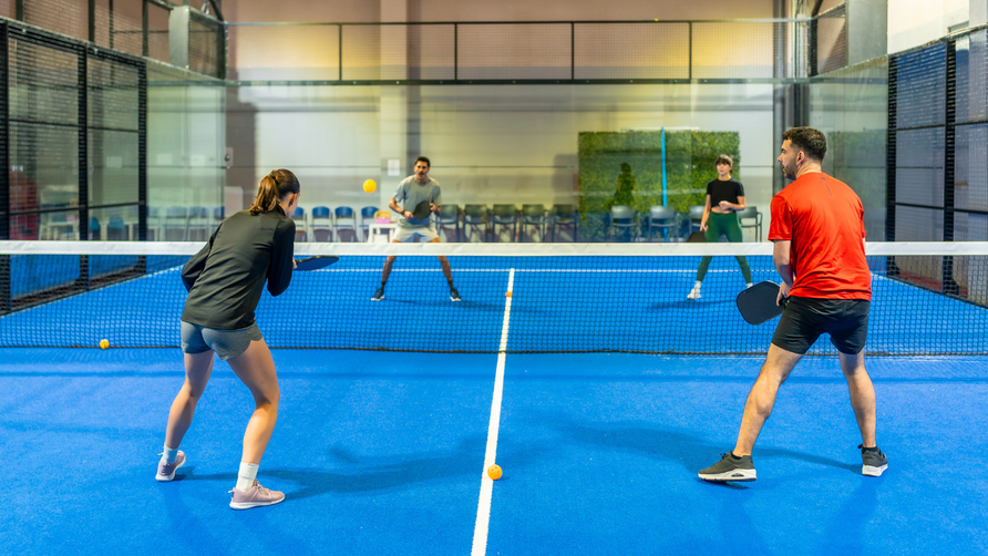 Groep padelspelers speelt dubbelwedstrijd op indoor padelbaan met glazen wanden