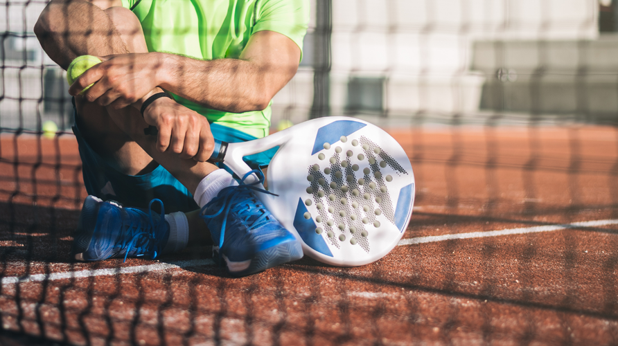 Beginner met armklachten op padelbaan houdt onderarm vast naast padelracket