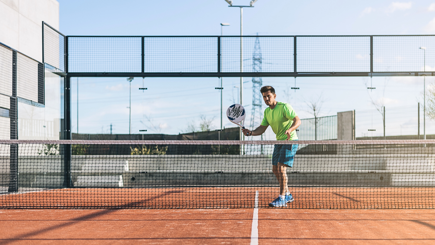 Padelspeler die een gecontroleerde slag uitvoert met padelracket op outdoor padelbaan
