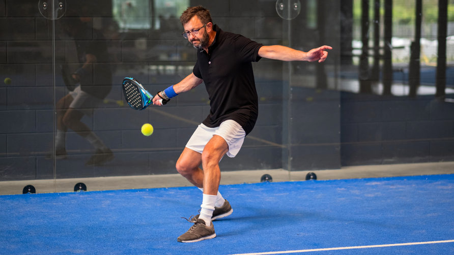 Padelspeler slaat bal met kracht met padelracket tijdens forehand slag