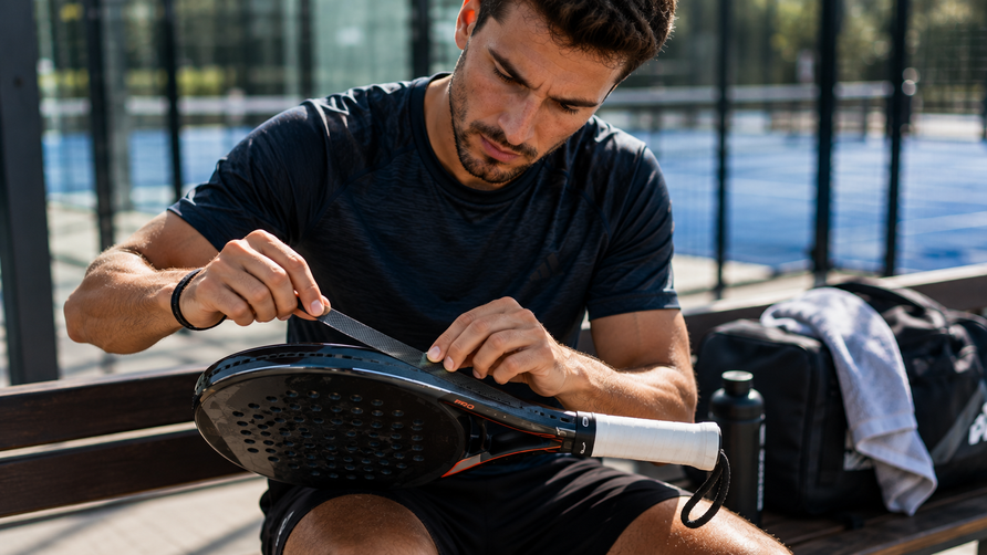 Padelspeler brengt een protector aan op de bovenrand van een padelracket ter bescherming tegen krassen en lichte stoten